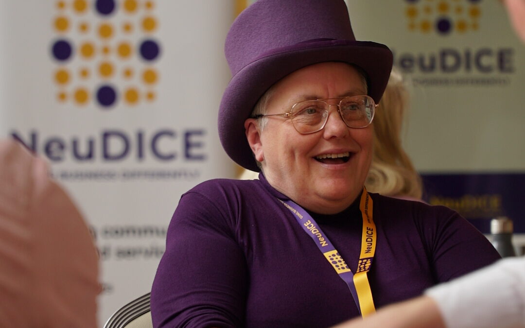 Anne Collins at the Neudice Launch event held at Plymouth Council House. Anne is wearing her purple top hat and has abroad smile on her face while conversing with attendees.
